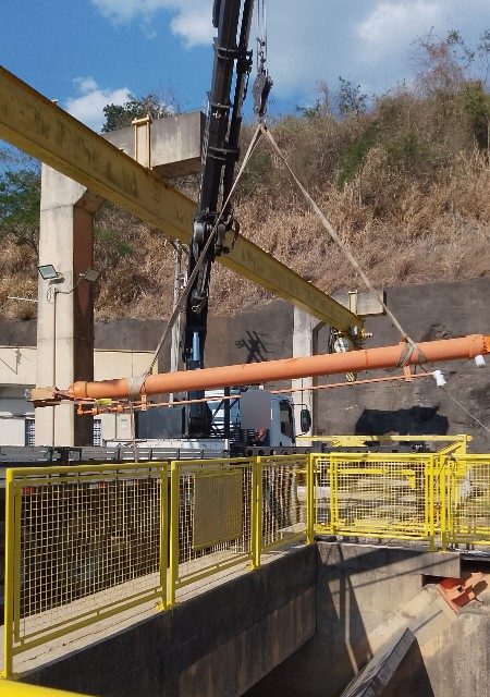 Caminhão munck içando cilindro da comporta de usina hidrelétrica, com cintas, sob pórtico