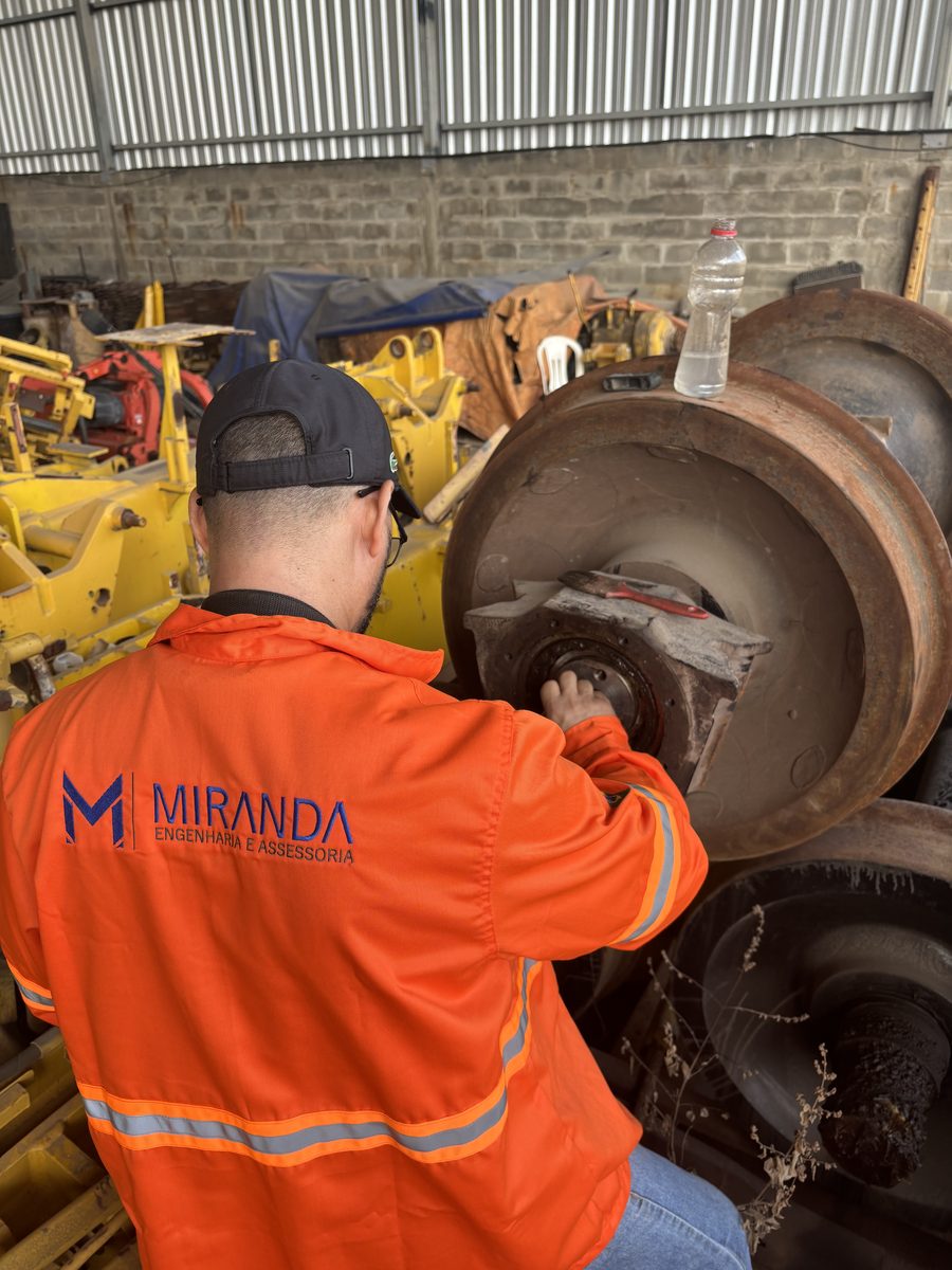 Inspetor de jaqueta laranja com a marca Miranda inspecionando rodeiro ferroviário por ultrassom